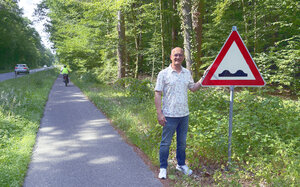 Man sieht B&uuml;rgermeister W&uuml;nstel auf dem Radweg an der K 10. Neben ihm ein Schild, rot mit einem Dreieck, in der Mitte sieht man zwei Wellen. Das Schild zeigt an "Vorsicht, der Radweg ist uneben und evtl. gef&auml;hrlich".
