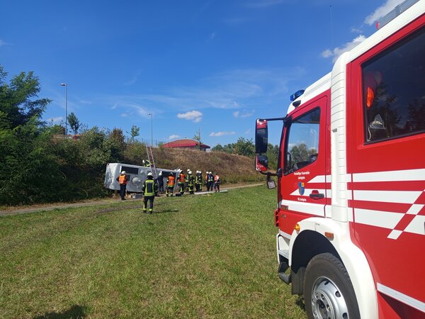 Das Foto zeigt vorne rechts ein Feuerwehrauto. Im hinteren Teil des Fotos sieht man die Feuerwehr beim Einsatz