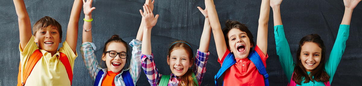 Bild vergrößern: Kinder stehen vor einer Schultafel und halten die Hände in die Höhe.